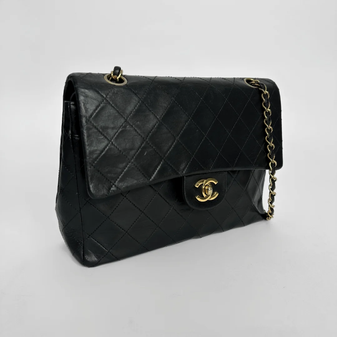 Black quilted handbag with gold chain and clasp on a light gray background