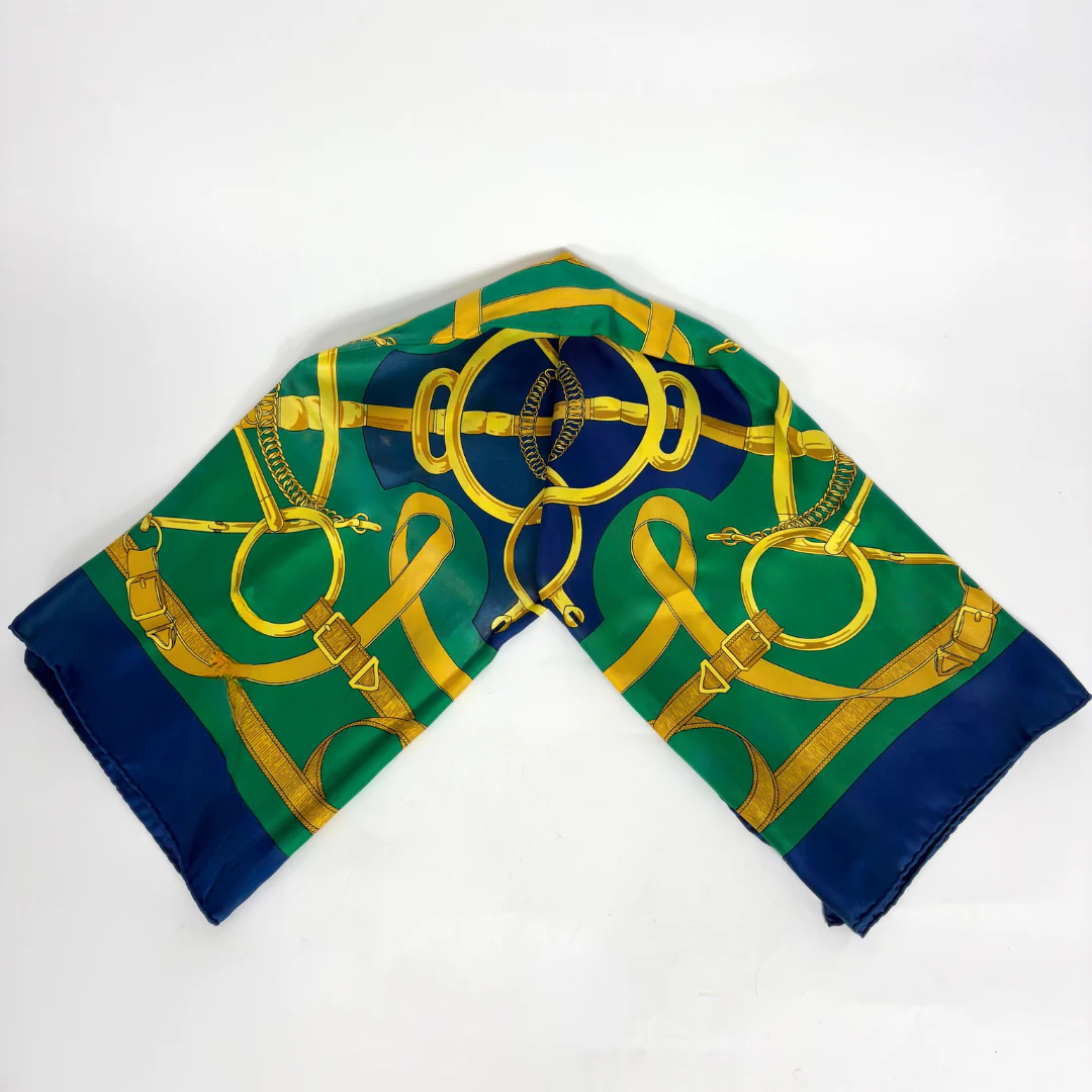 Folded green and blue scarf with gold horsebit pattern on a white background