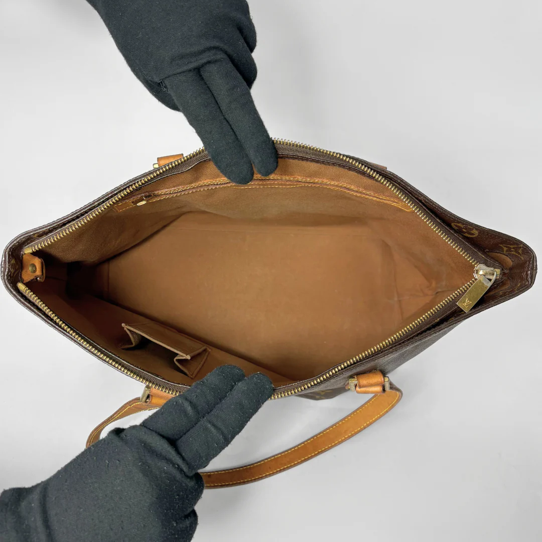 Brown leather handbag with open zipper held by gloved hands on a white background