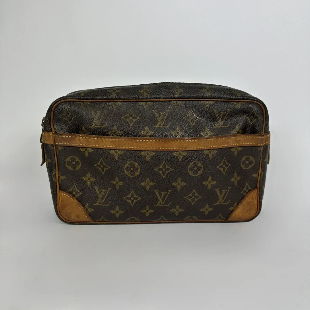A Louis Vuitton monogram toiletry bag in brown coated canvas with tan leather trim and corner patches, shown against a plain light gray background.