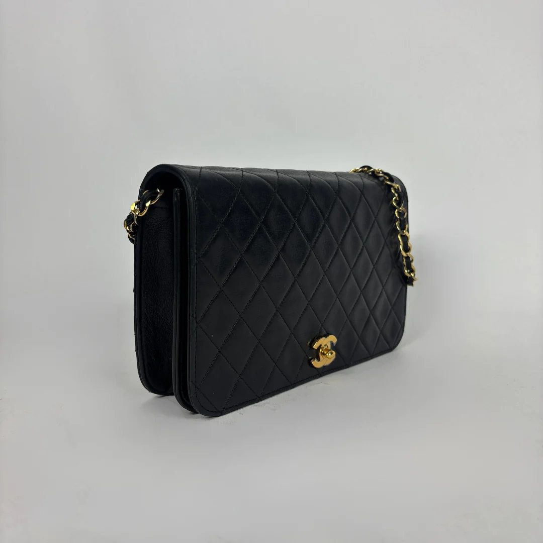 A black quilted leather shoulder bag with gold-tone hardware, featuring a diamond-quilted pattern and a small interlocking CC turn-lock closure on the front flap, photographed against a neutral light gray background.