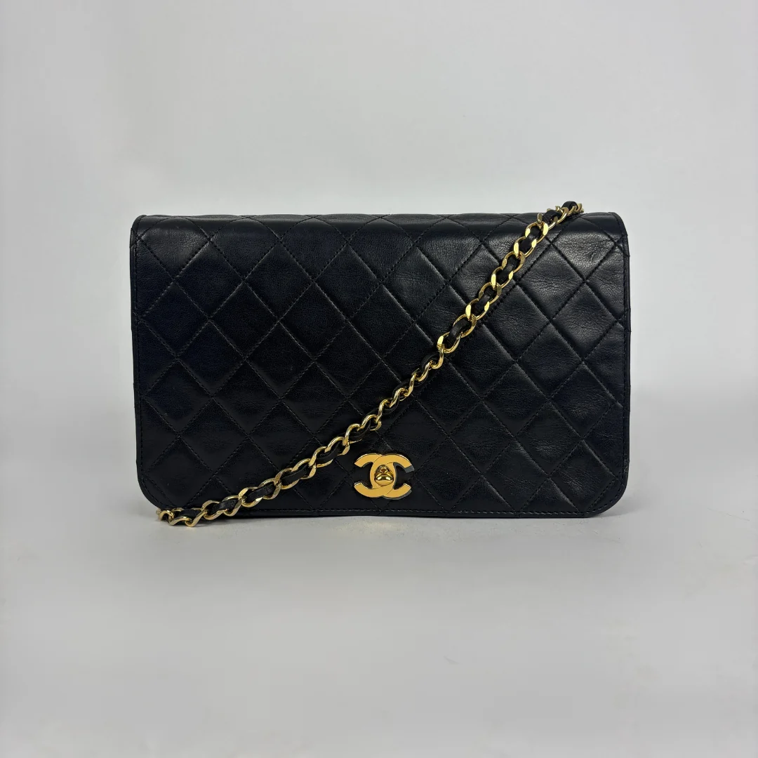 A black quilted leather shoulder bag with a gold-tone chain strap and a gold interlocking CC logo, photographed against a neutral light gray background.