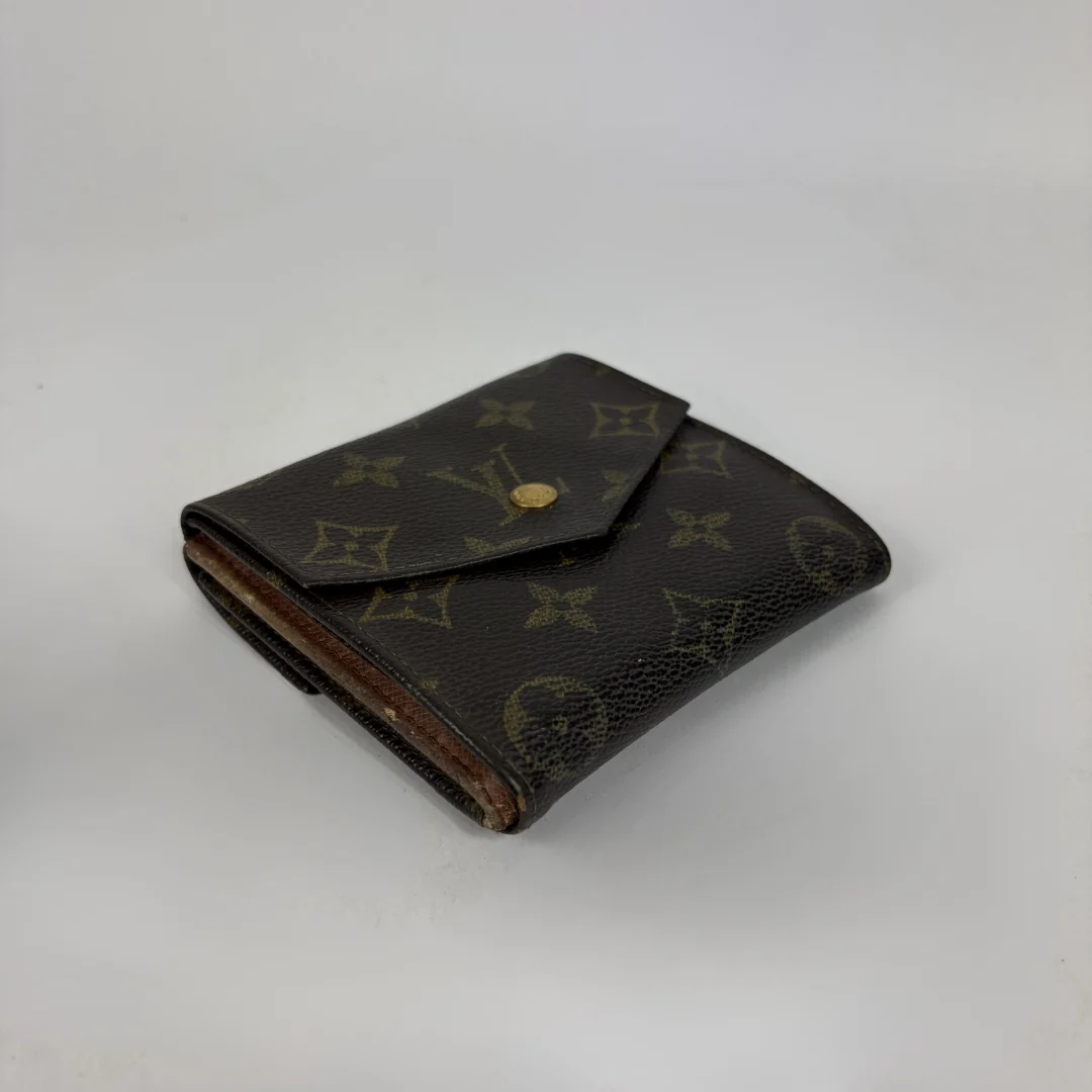 A classic Louis Vuitton monogram bifold wallet in dark brown coated canvas with gold-tone hardware, photographed on a neutral light gray background.