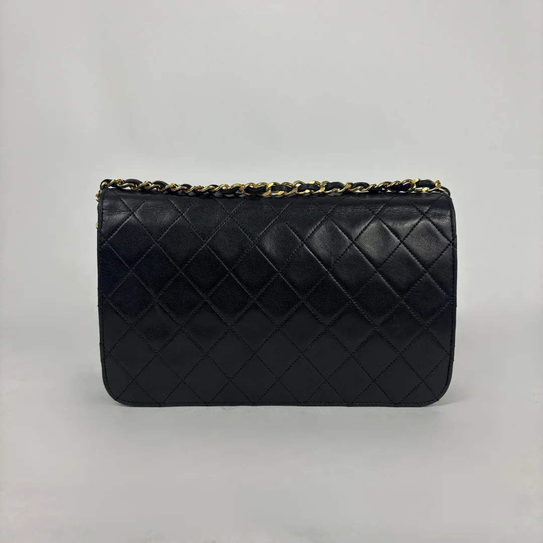 A black quilted leather clutch bag with a gold-tone chain strap, photographed against a neutral light gray background.