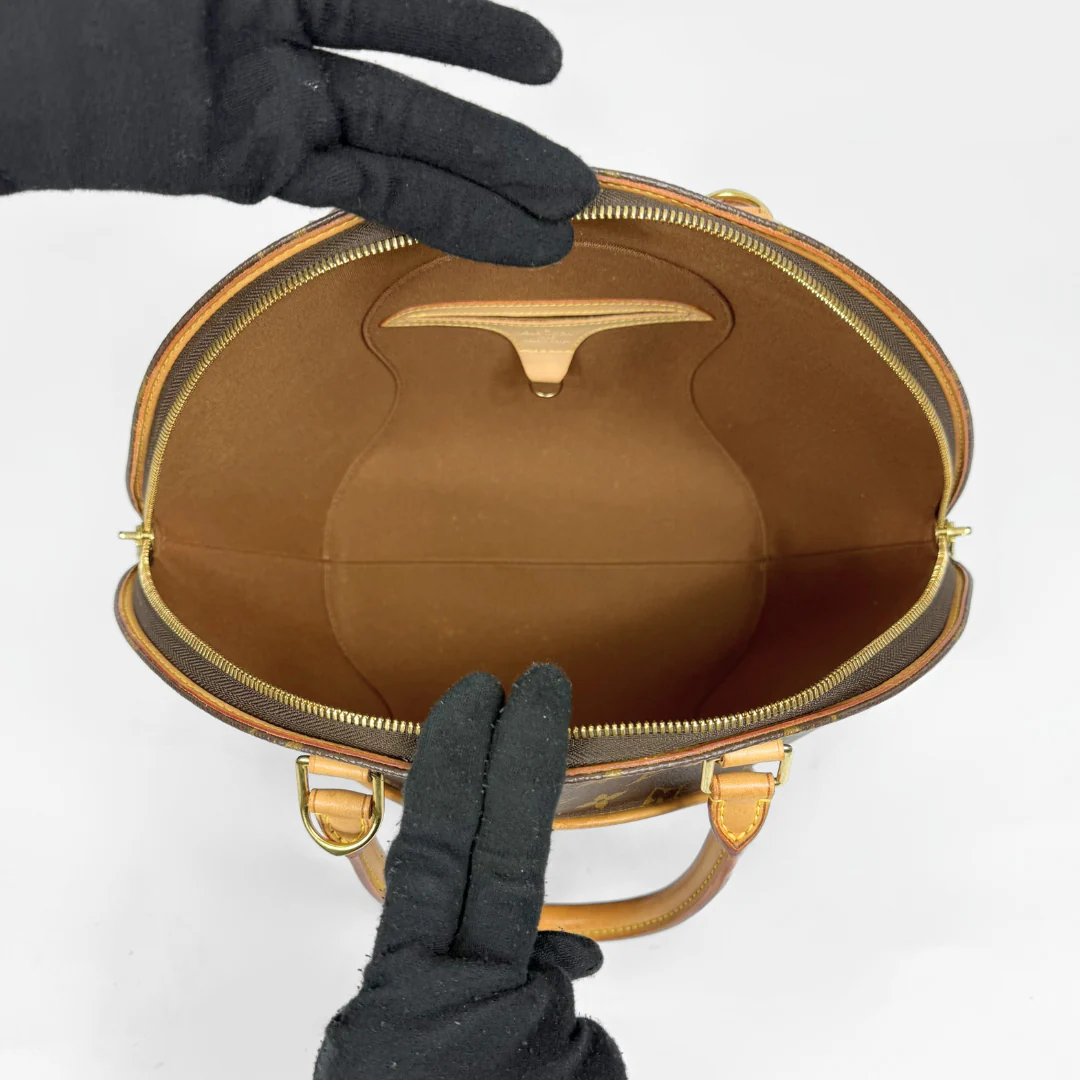 Brown handbag with gold accents held by a gloved hand on a white background