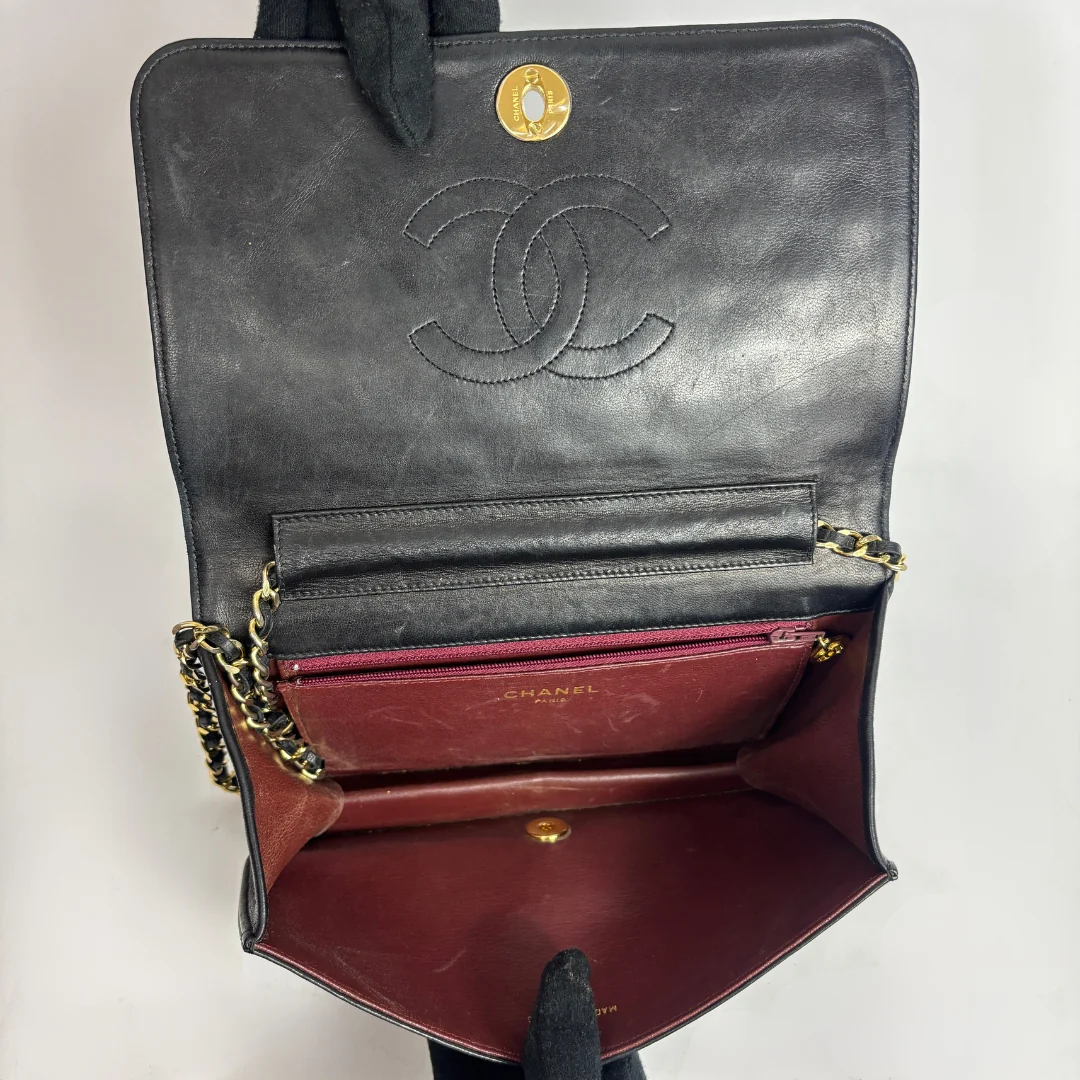 An open Chanel shoulder bag in black leather, showing the interior with a burgundy-red lining, gold-tone chain strap, and the embossed Chanel logo on the inside flap.