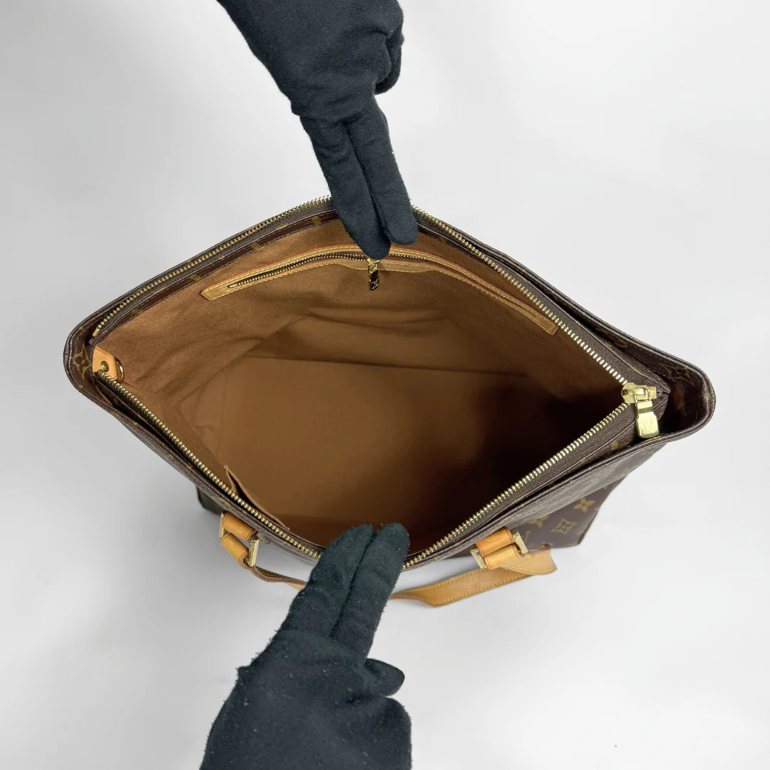 Brown leather bag with gold zipper being held open by gloved hands on a light gray background
