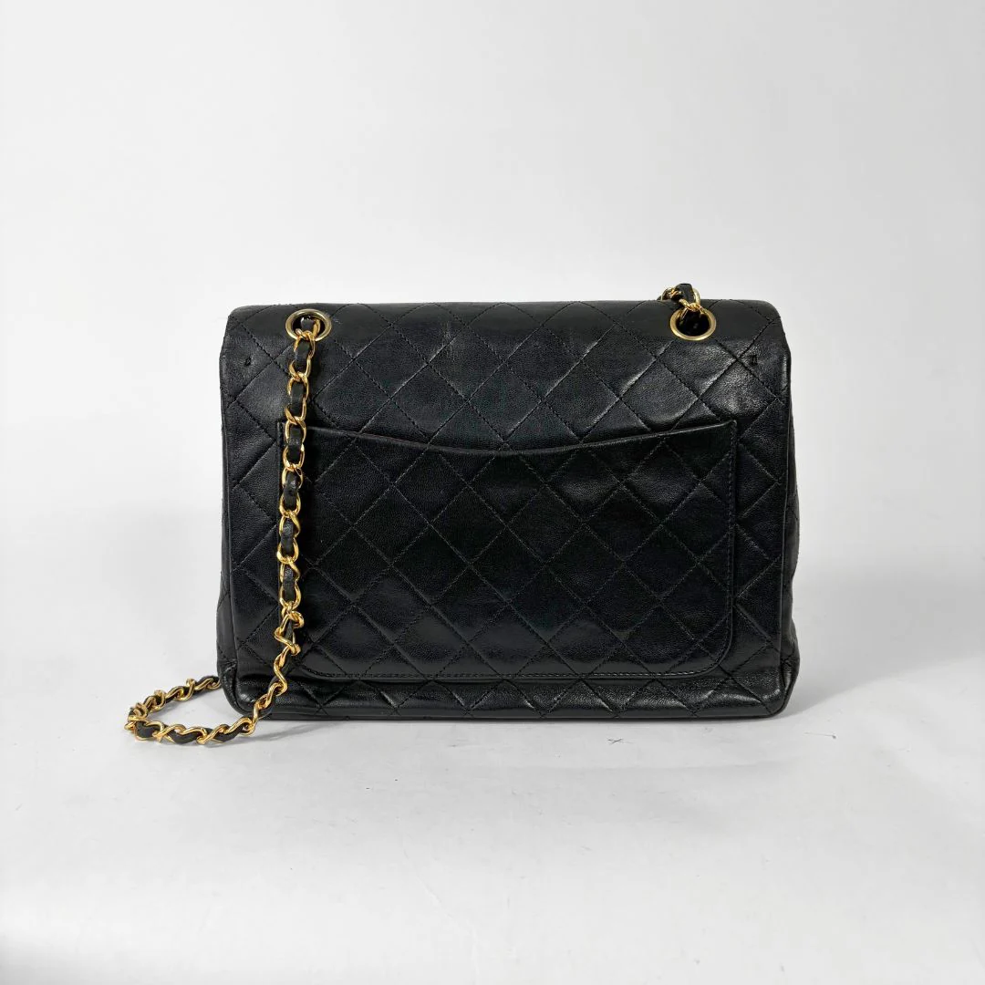 Black quilted handbag with gold chain and clasp on a white background