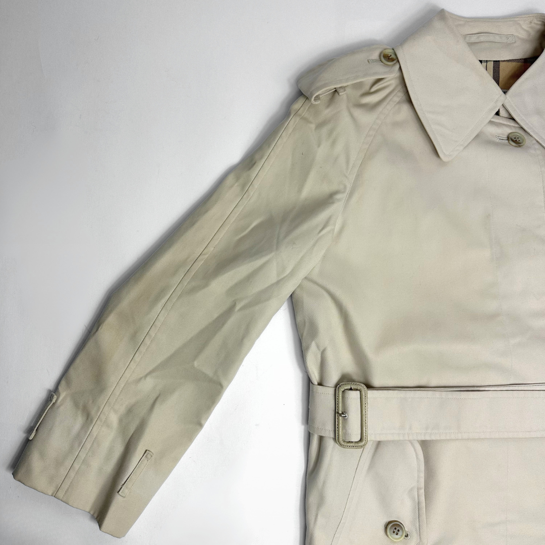 Beige trench coat on a mannequin against a gray background