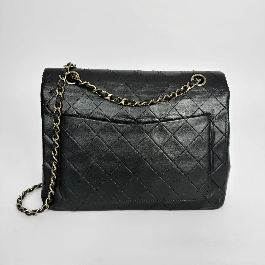 Black quilted handbag with gold chain on a light gray background