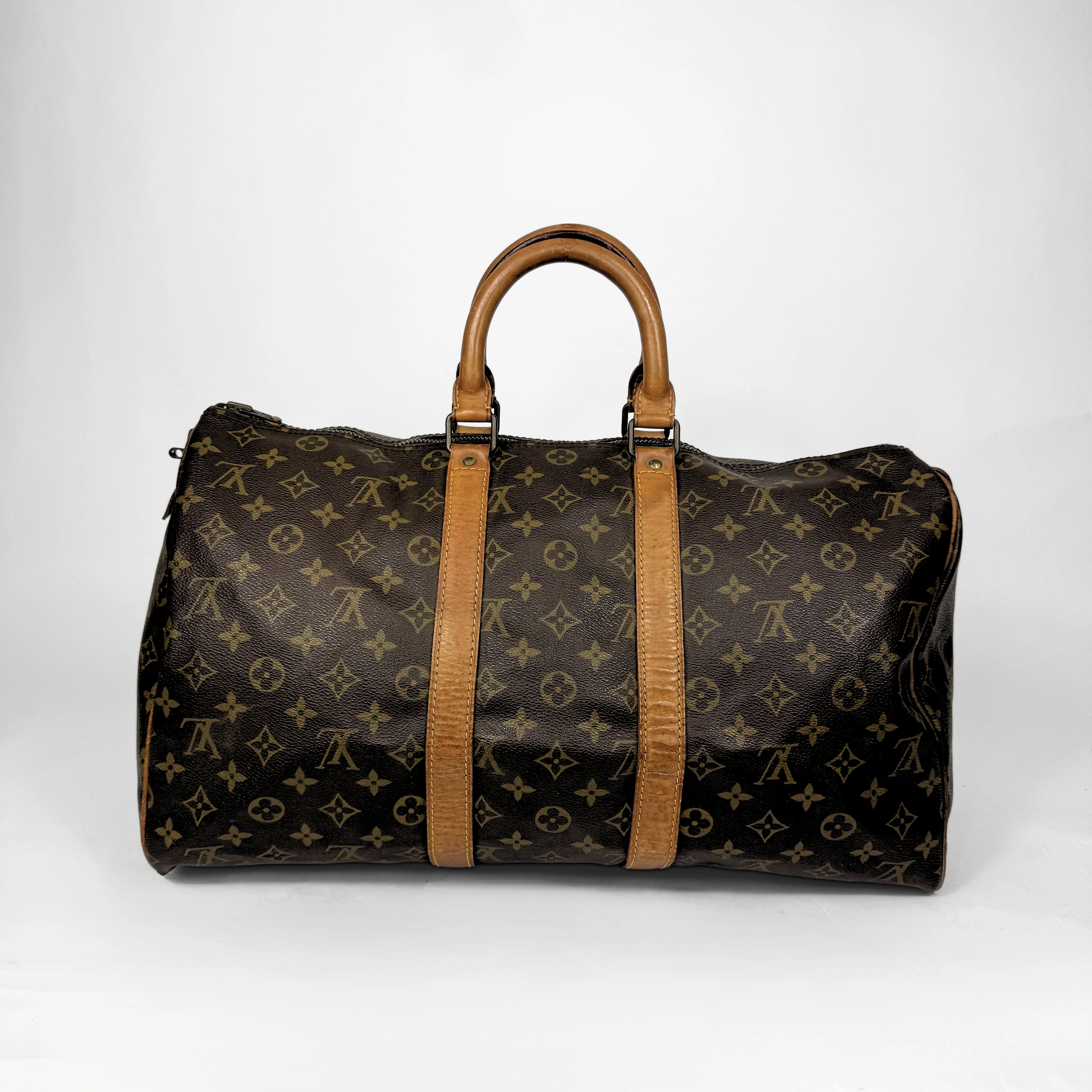 Brown duffel bag with tan handles and monogram pattern on a white background