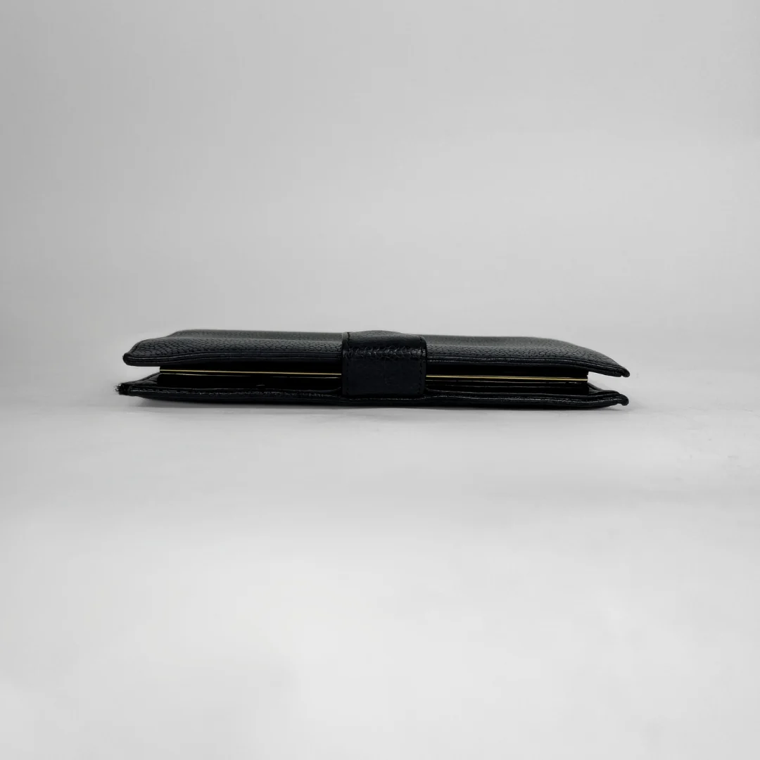 A black textured leather wallet with a matching black strap closure, shown closed on a neutral light gray background.