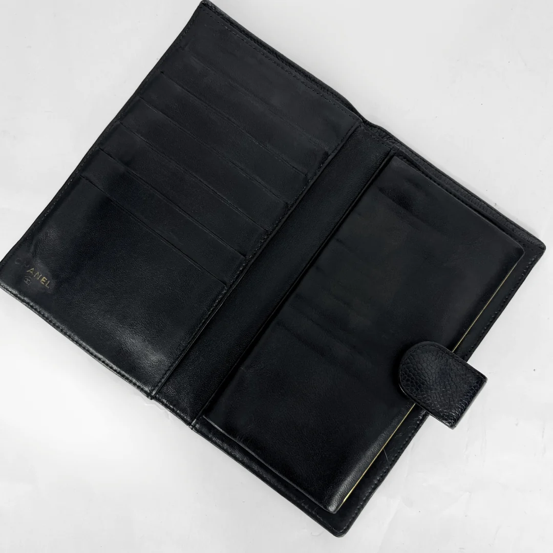 An open black leather wallet or bifold with multiple card slots and a small embossed brand mark on the left panel, photographed on a light neutral background.
