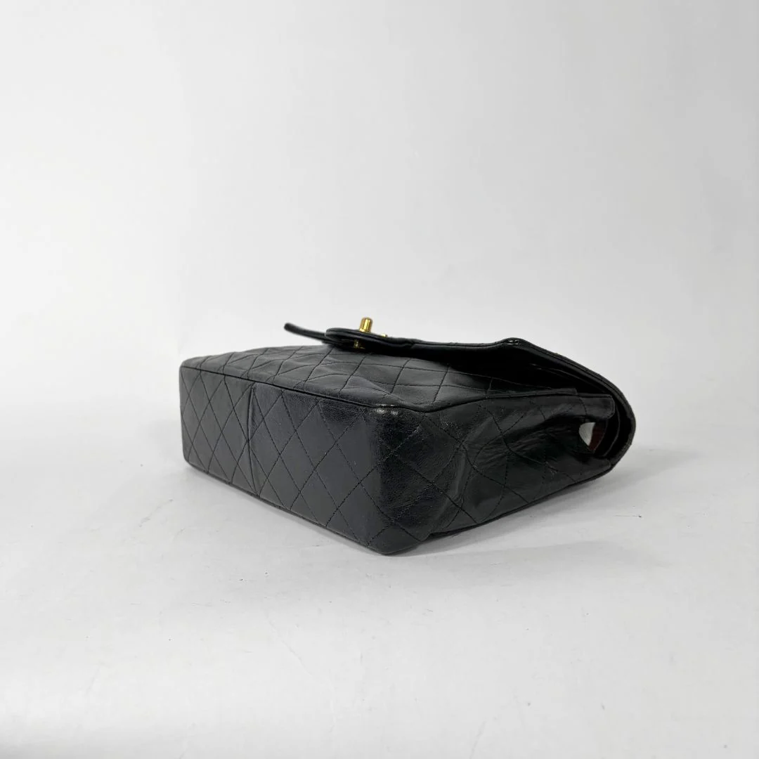 Black quilted handbag with gold chain and clasp on a white background