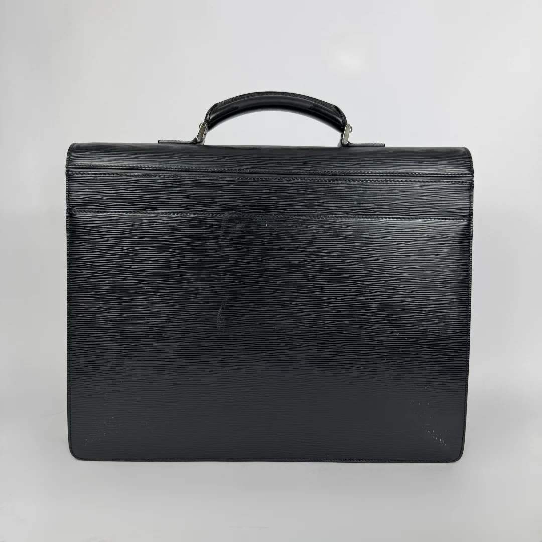 A black textured leather briefcase with a top handle, photographed against a neutral light gray background.
