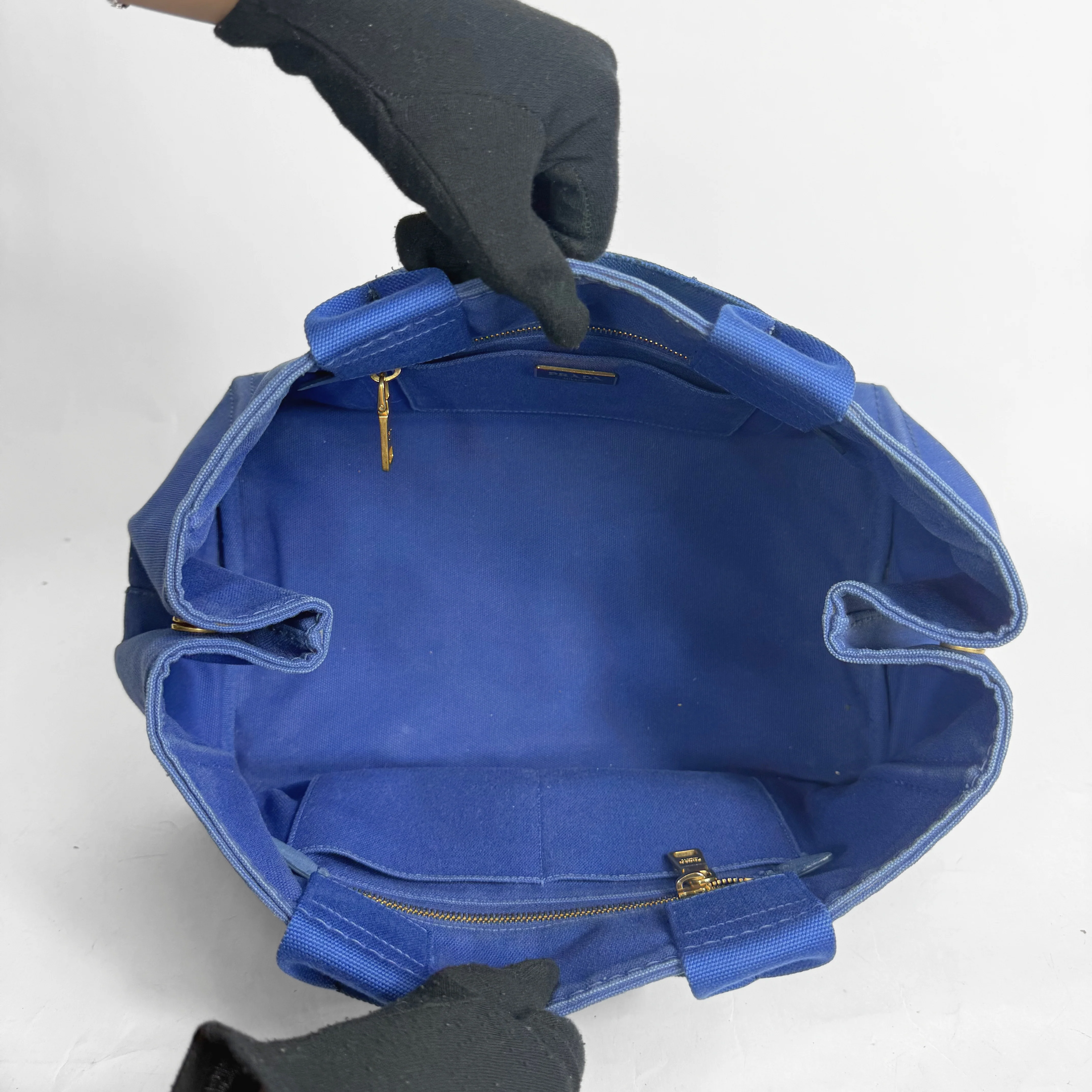 Blue bag with gold zippers held open by a gloved hand on a white background