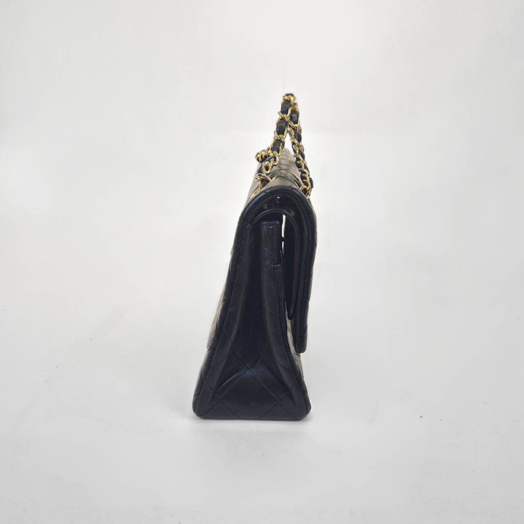 Black Chanel handbag with gold chain handle and clasp on a white background