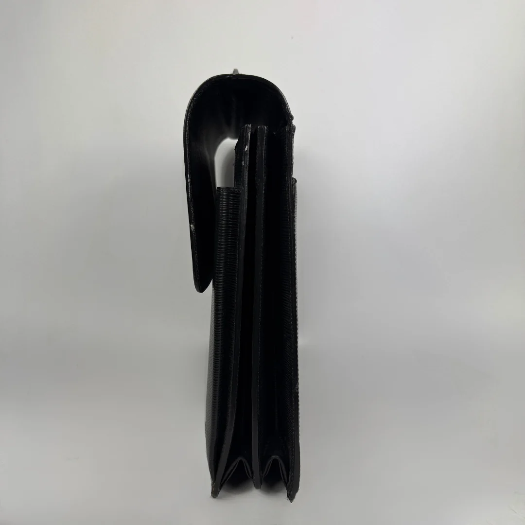 A black leather wallet shown from the side profile, featuring a smooth leather flap and a textured elastic band, set against a plain light gray background.