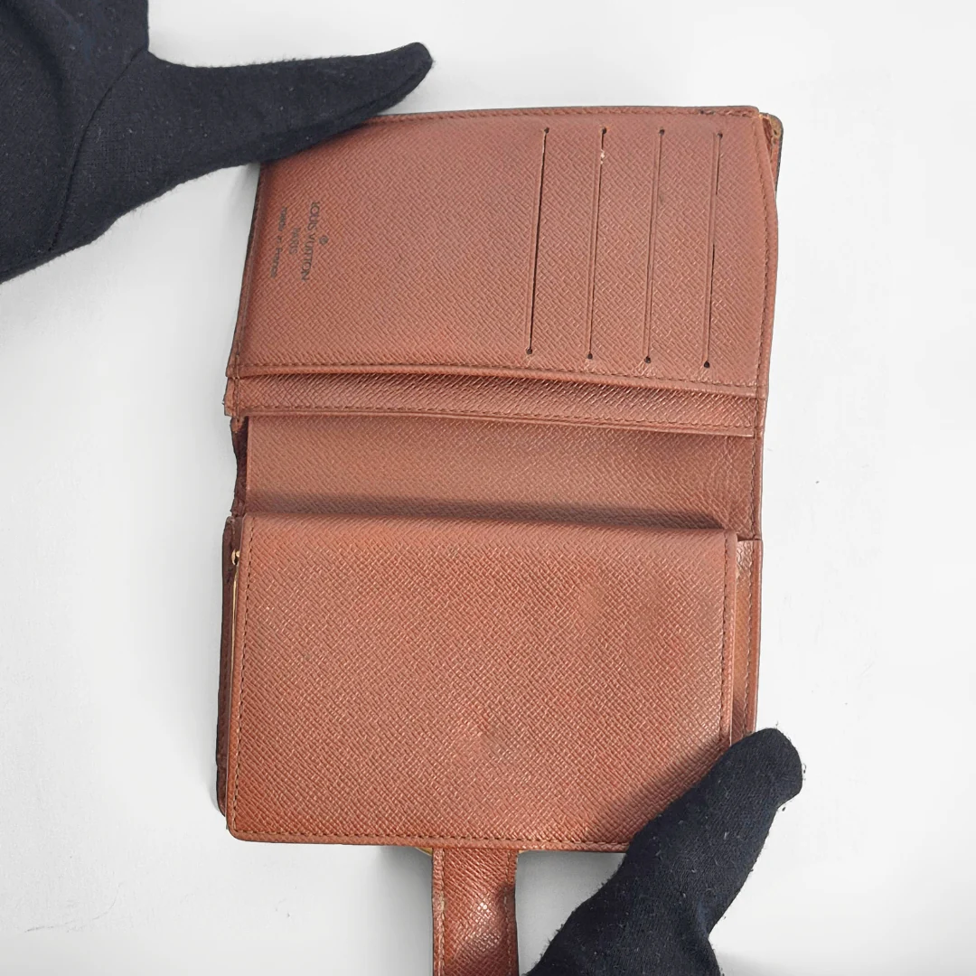 Brown textured wallet held by a gloved hand on a white background