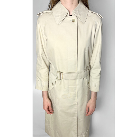 Beige trench coat worn by a person on a plain background