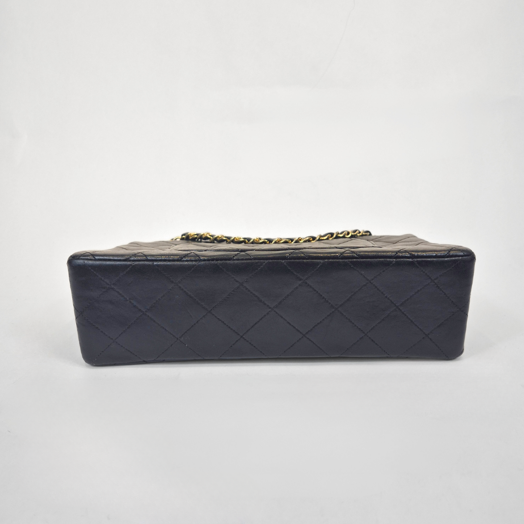 Black Chanel handbag with gold chain handle and clasp on a white background
