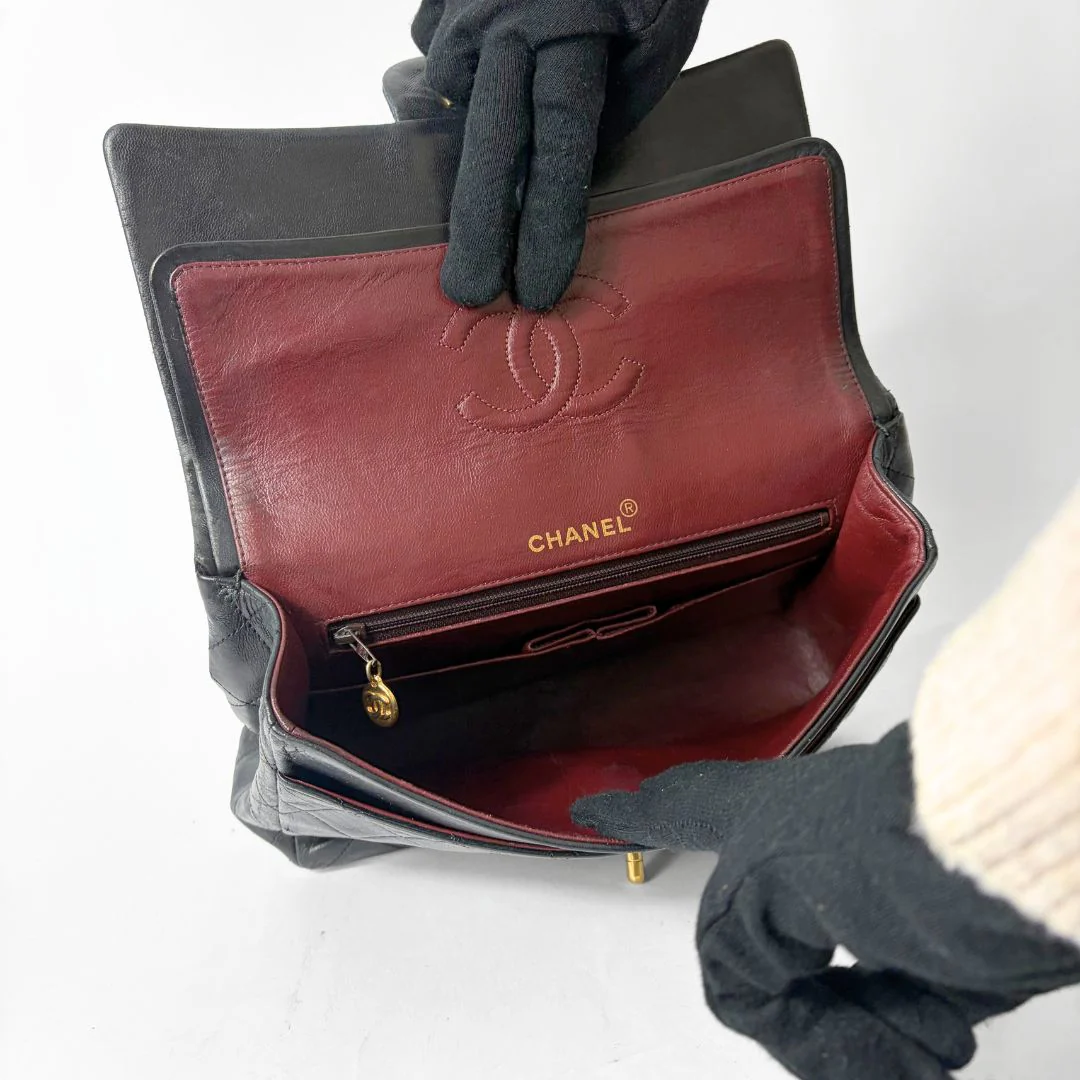 Black quilted handbag with gold chain and clasp on a white background