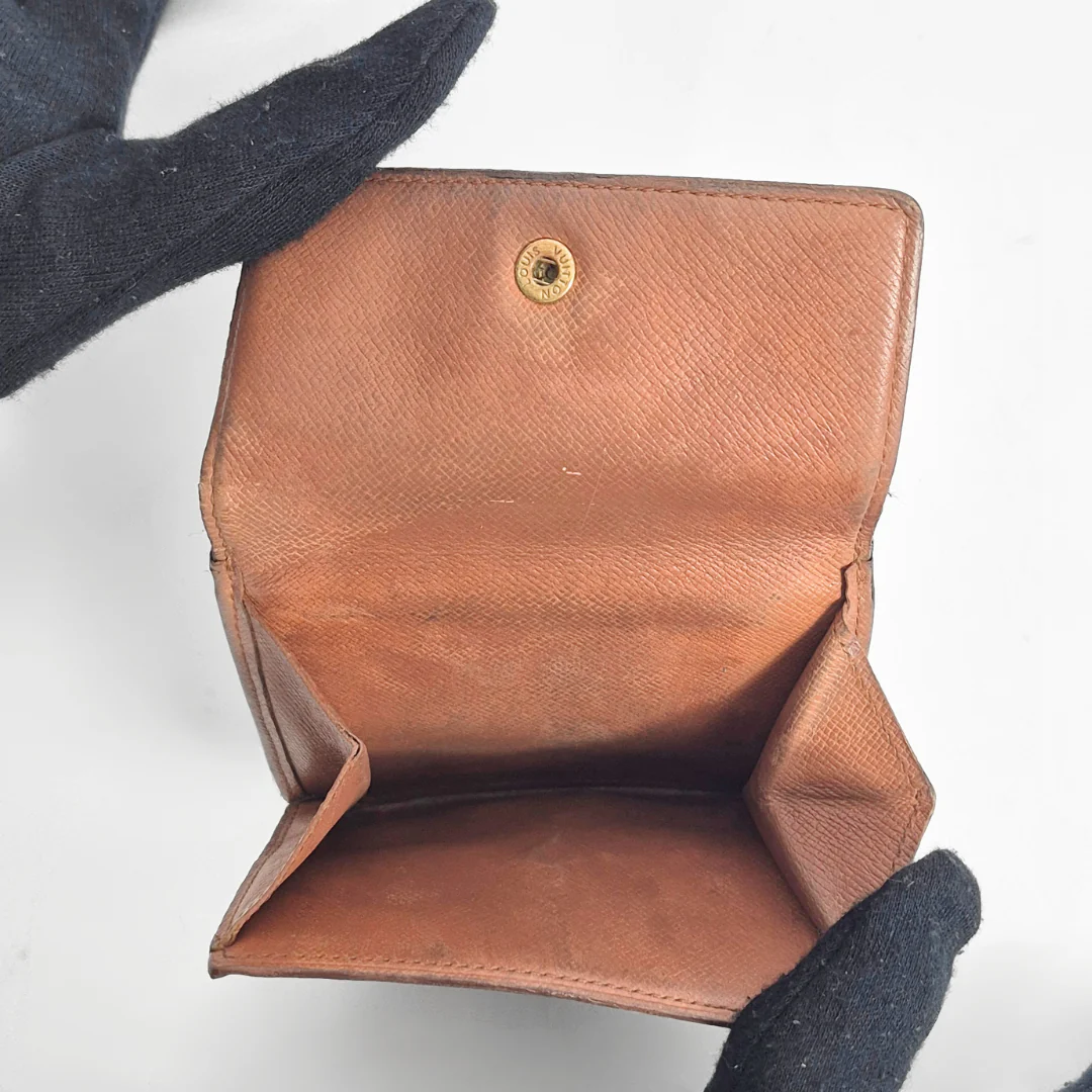 Brown leather wallet held open by a gloved hand on a white background