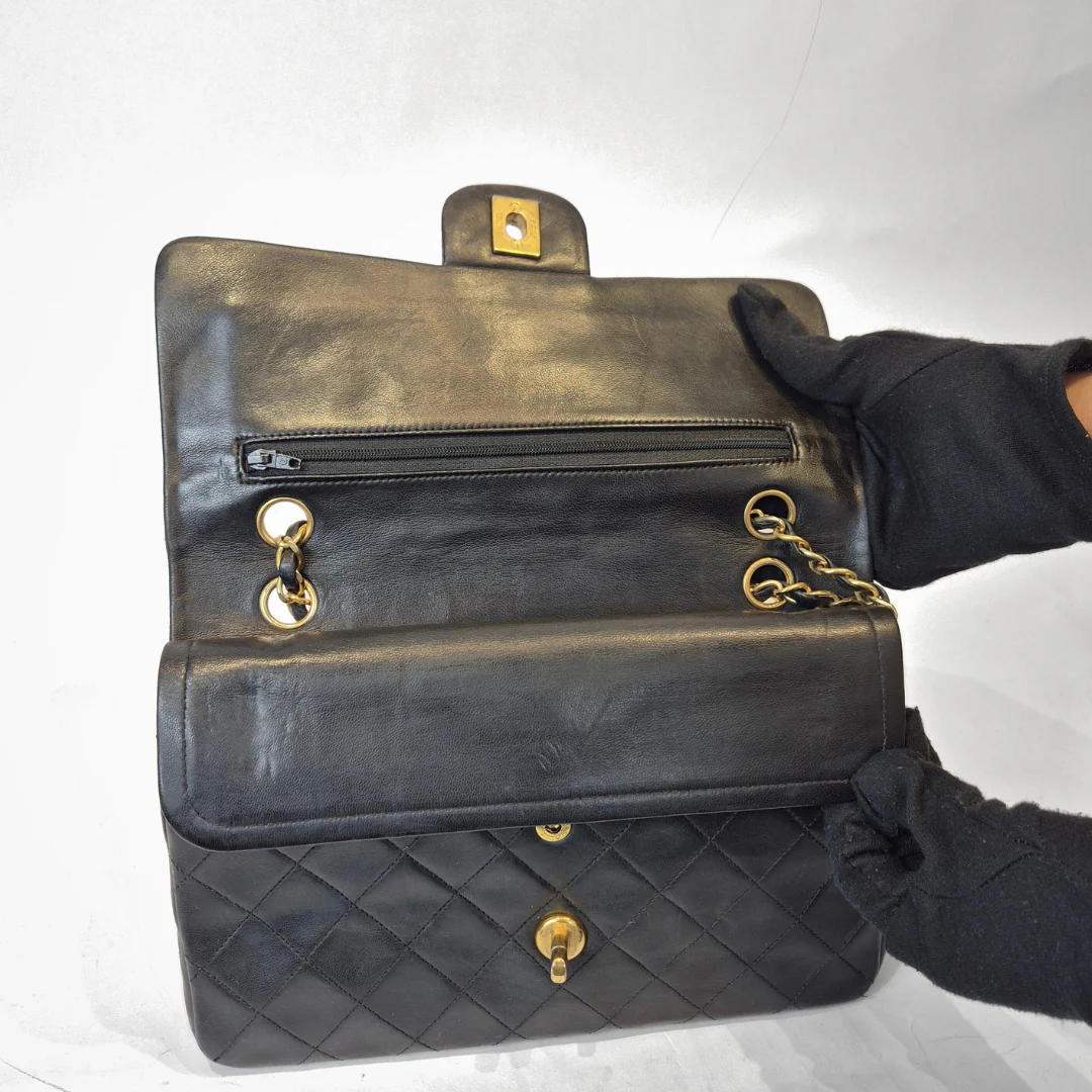 Black quilted handbag with gold hardware held by a gloved hand on a white background