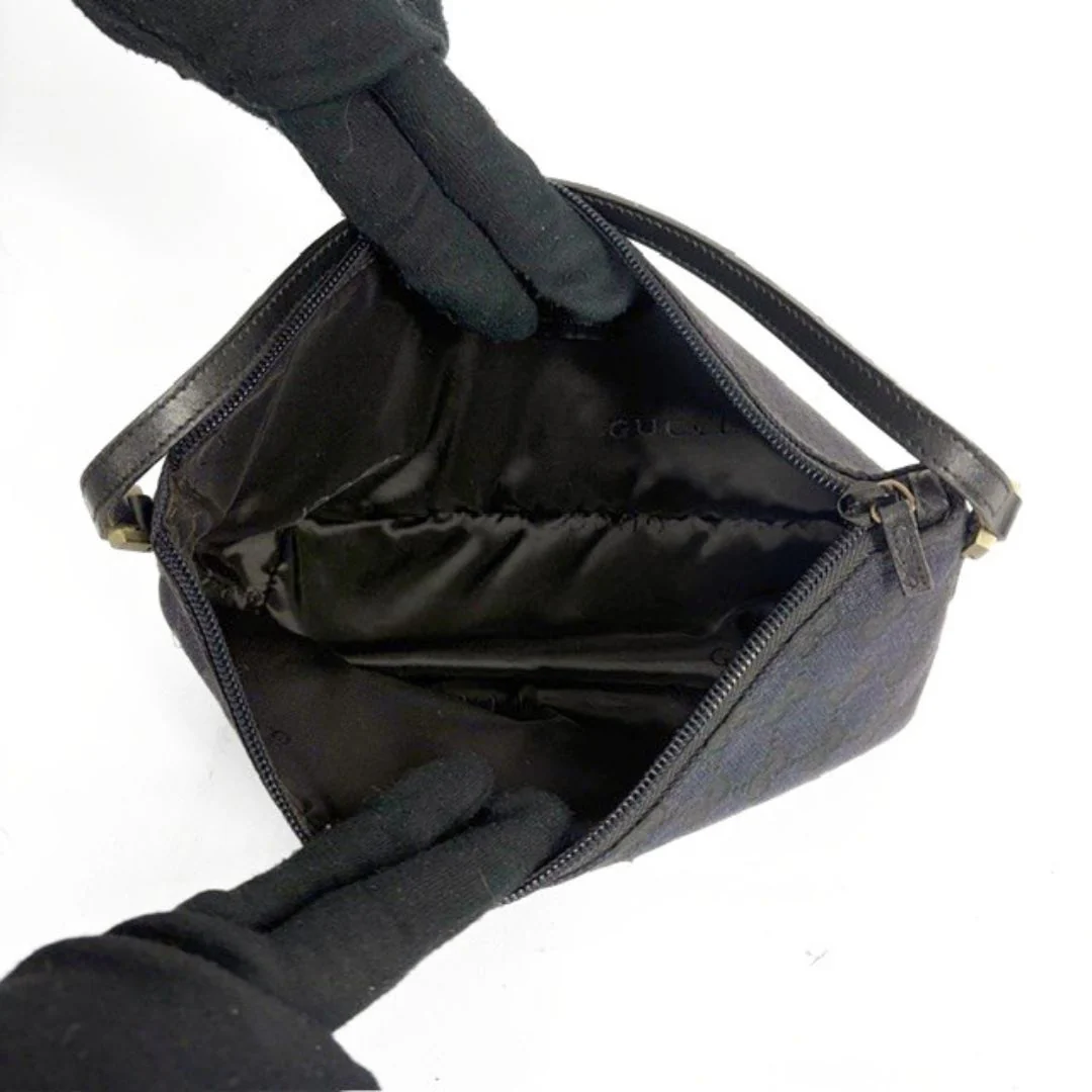 Black handbag with open lid held by gloved hands on a white background