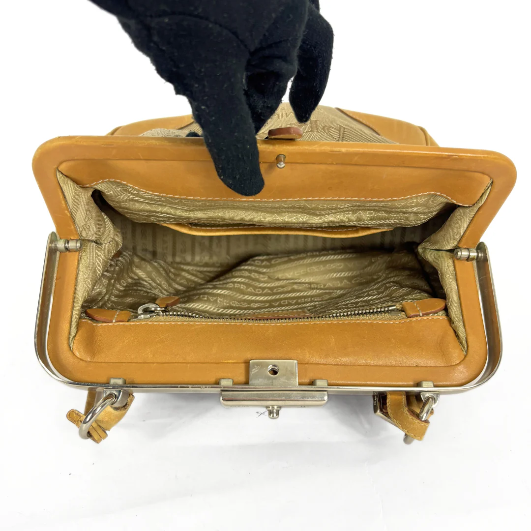 Tan handbag with gold interior being held open by a black-gloved hand on a white background