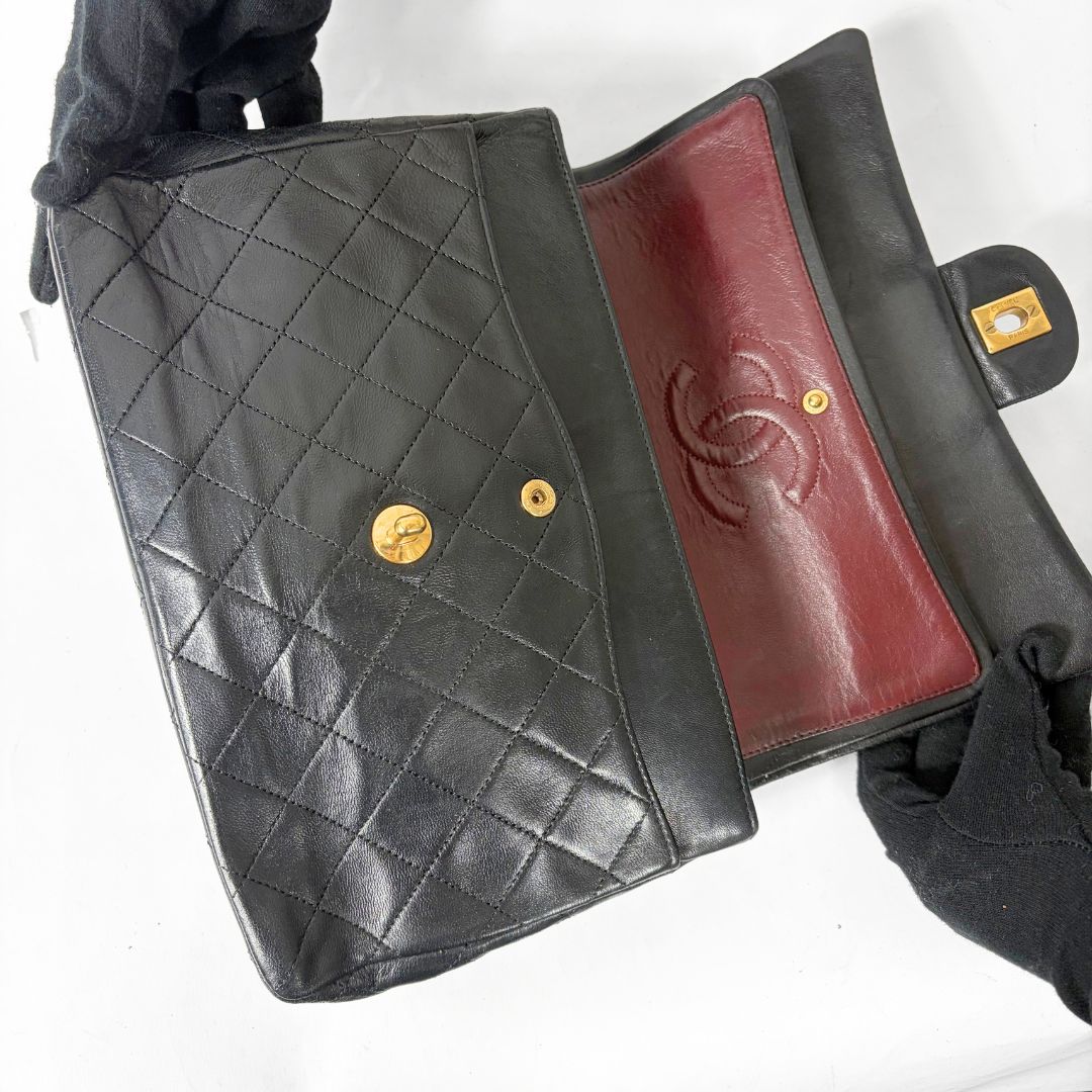Black quilted handbag with gold chain and clasp on a white background