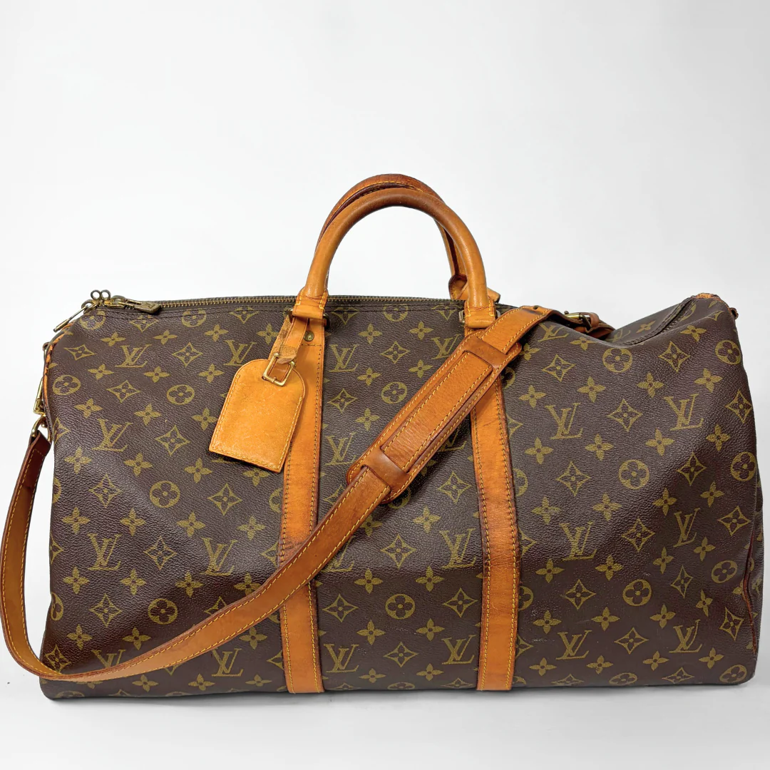 Brown monogram patterned travel bag with tan leather handles and strap on a white background