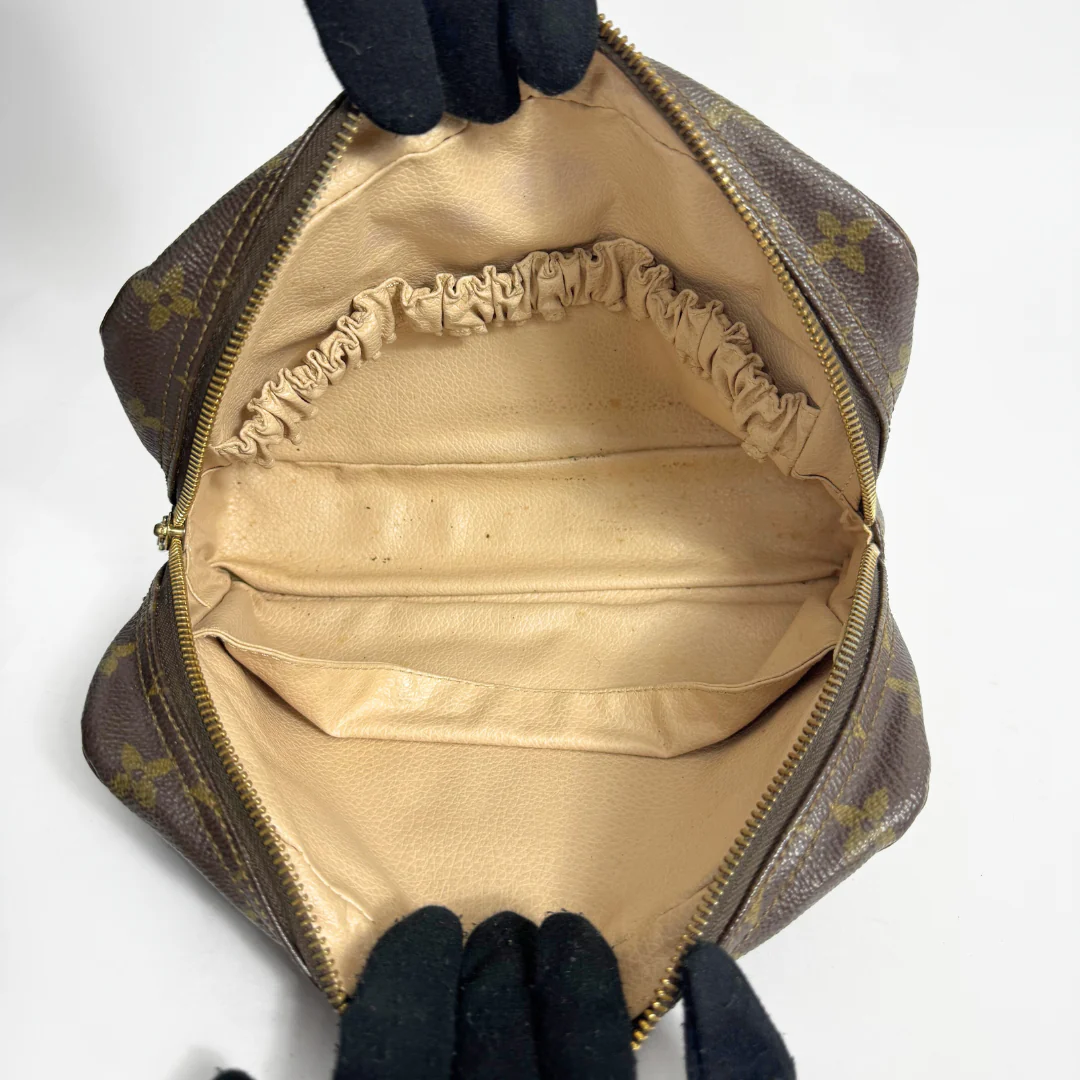 Open brown leather handbag with gold interior, held by gloved hands on a white background