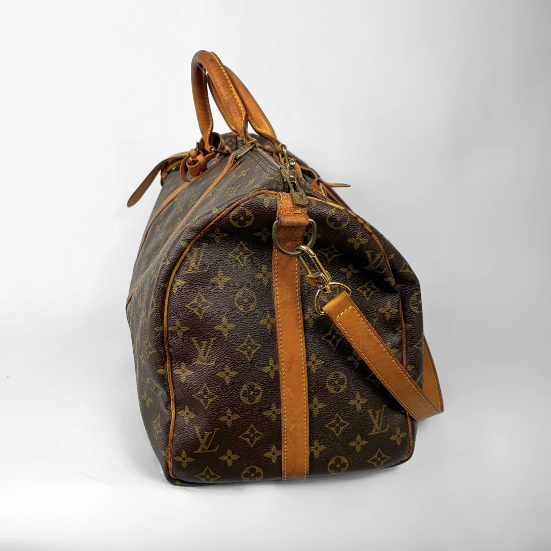 Brown monogram patterned travel bag with tan leather handles and strap on a white background