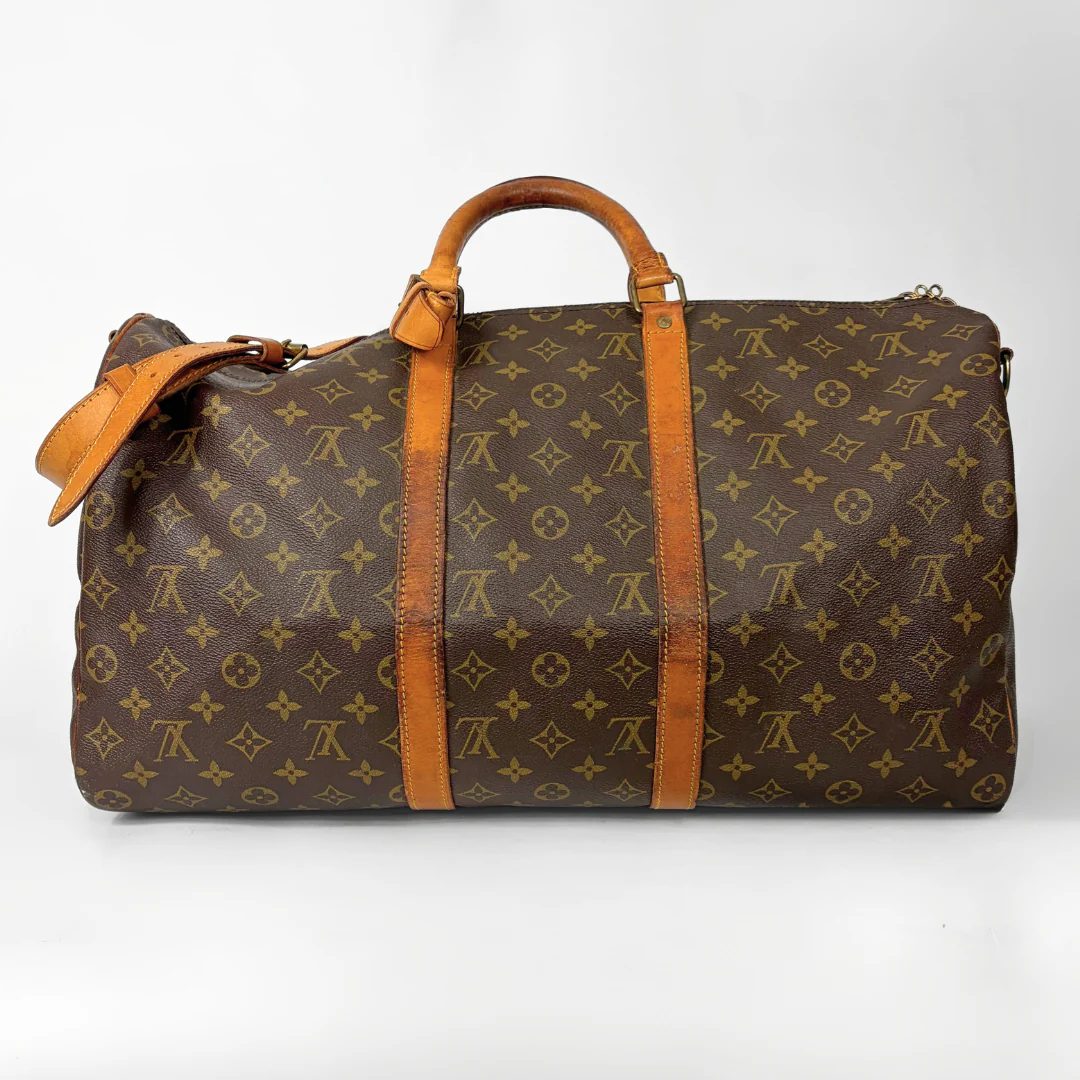 Brown monogram patterned travel bag with tan leather handles and strap on a white background