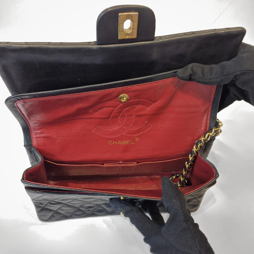 Black quilted handbag with red interior and Chanel logo, held open by a gloved hand.