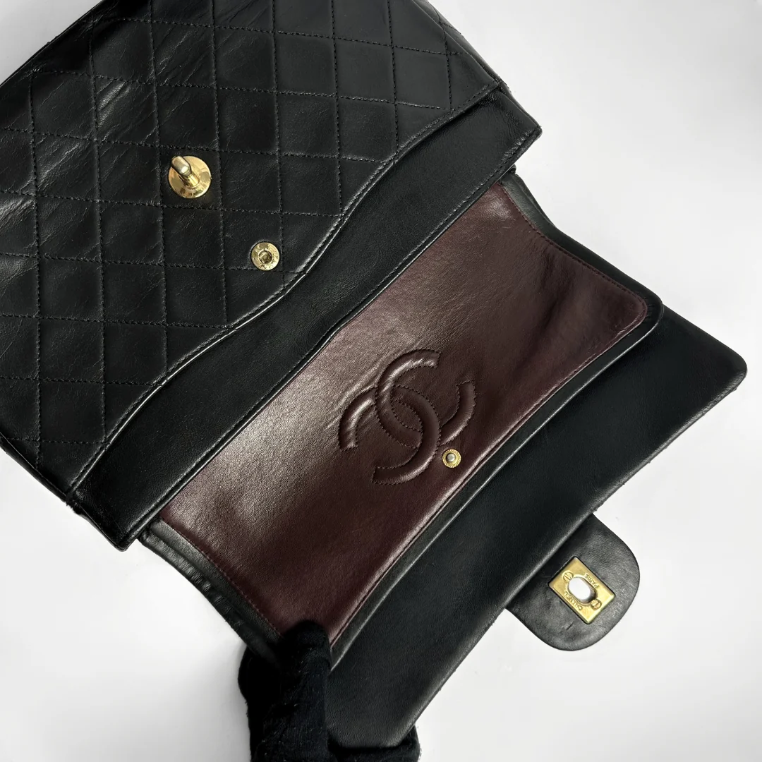 Black quilted handbag with brown leather flap and gold hardware on a white background