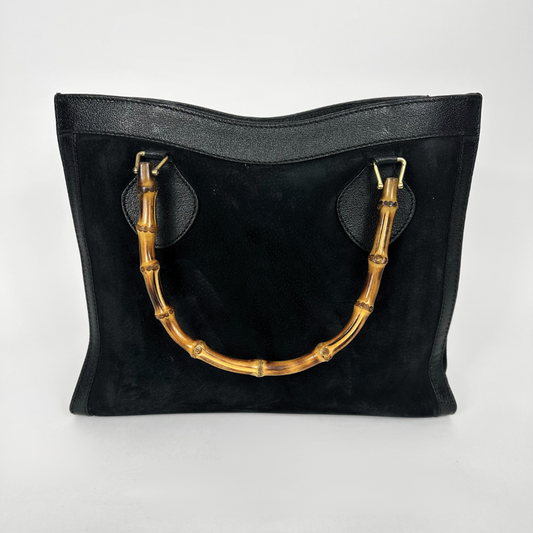 Black handbag with gold bamboo handles on a white background