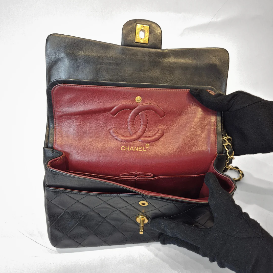 Black quilted handbag with red interior featuring Chanel logo, held open by a gloved hand.