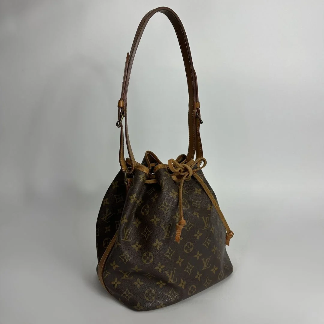 A Louis Vuitton monogram canvas bucket bag with a brown leather shoulder strap and drawstring closure, photographed against a neutral light gray background.