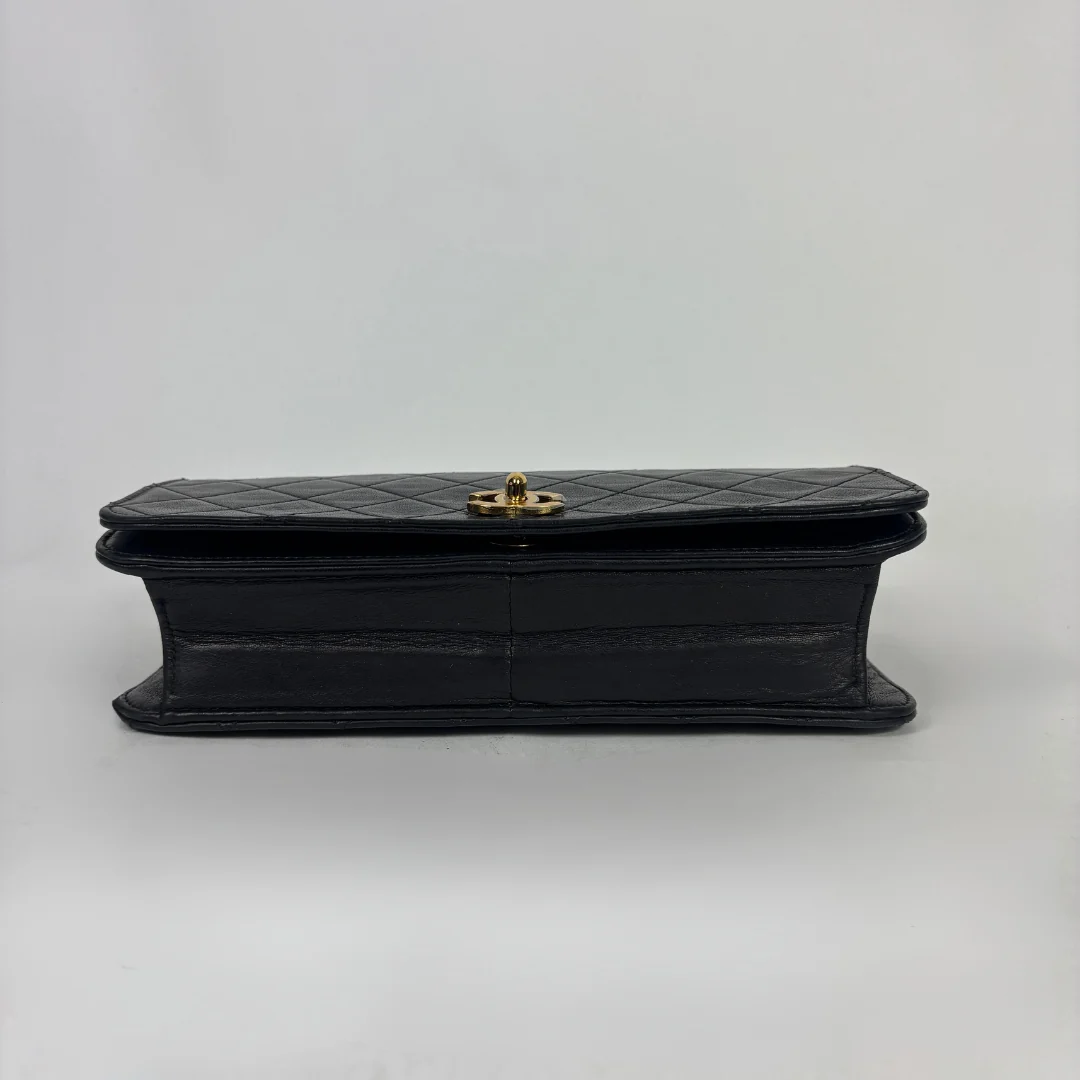 A black quilted leather clutch bag with a gold-tone turn-lock clasp, shown from the side against a plain light gray background.