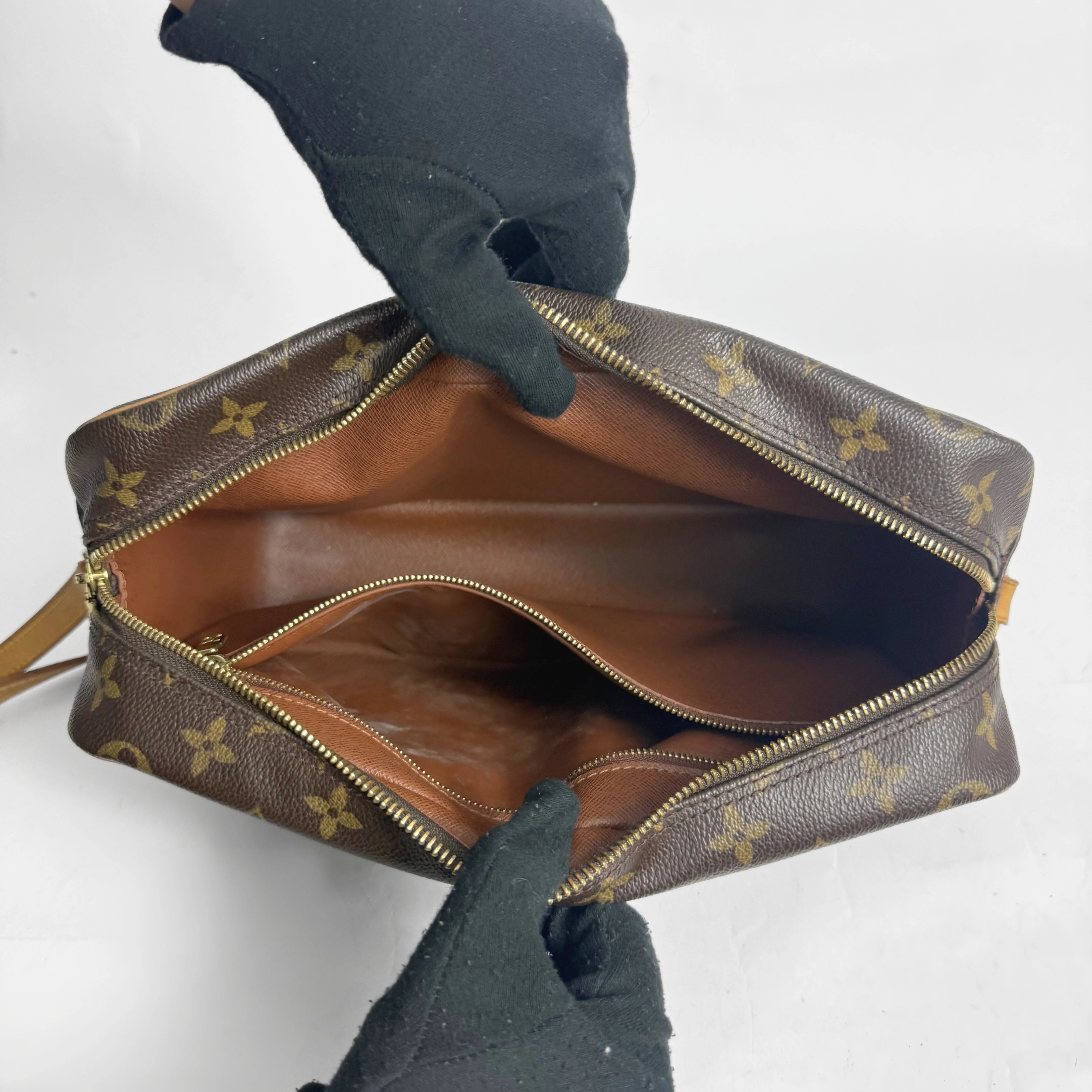 Brown handbag with gold monogram pattern held by gloved hands on a white background