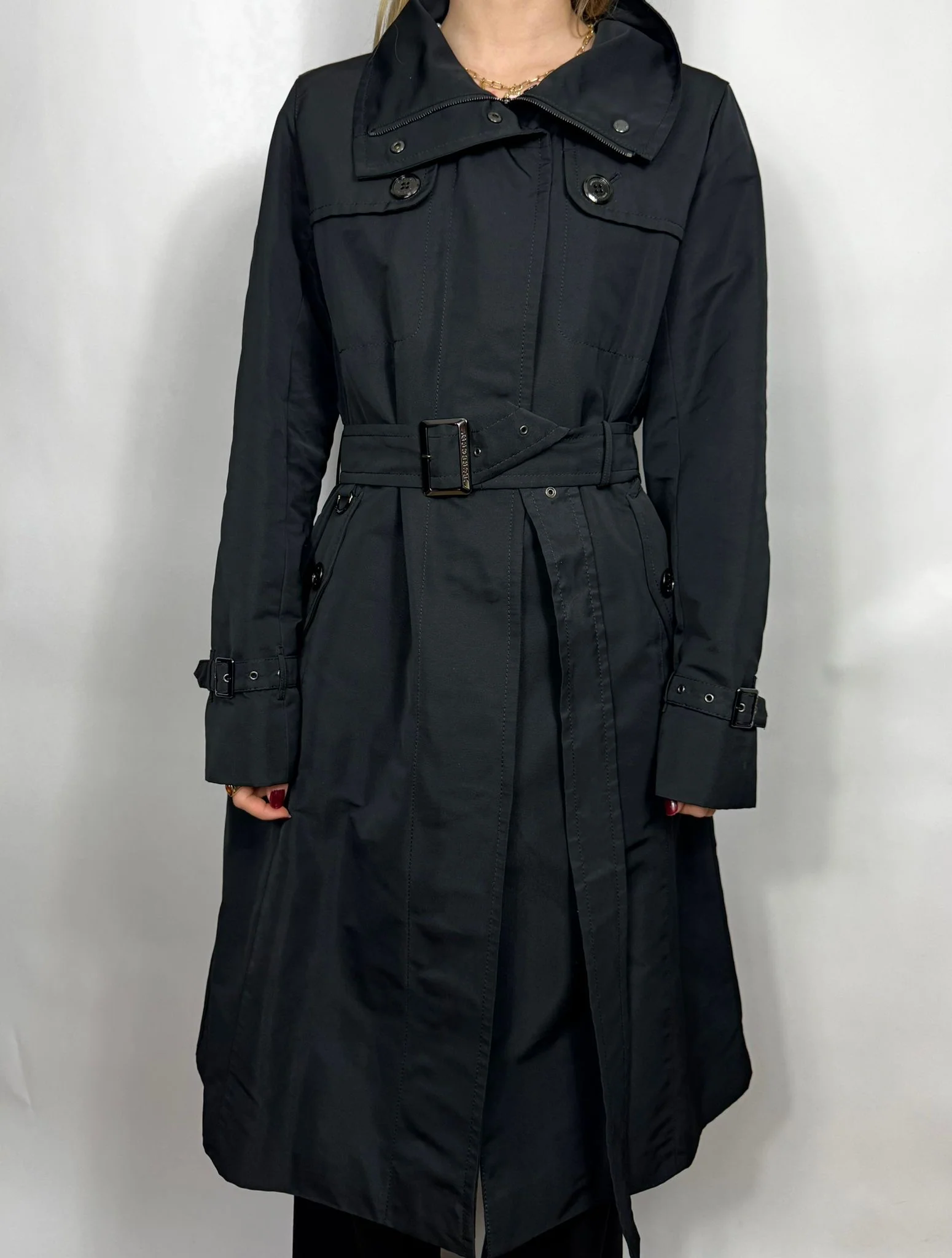 Black trench coat worn by a person on a plain background