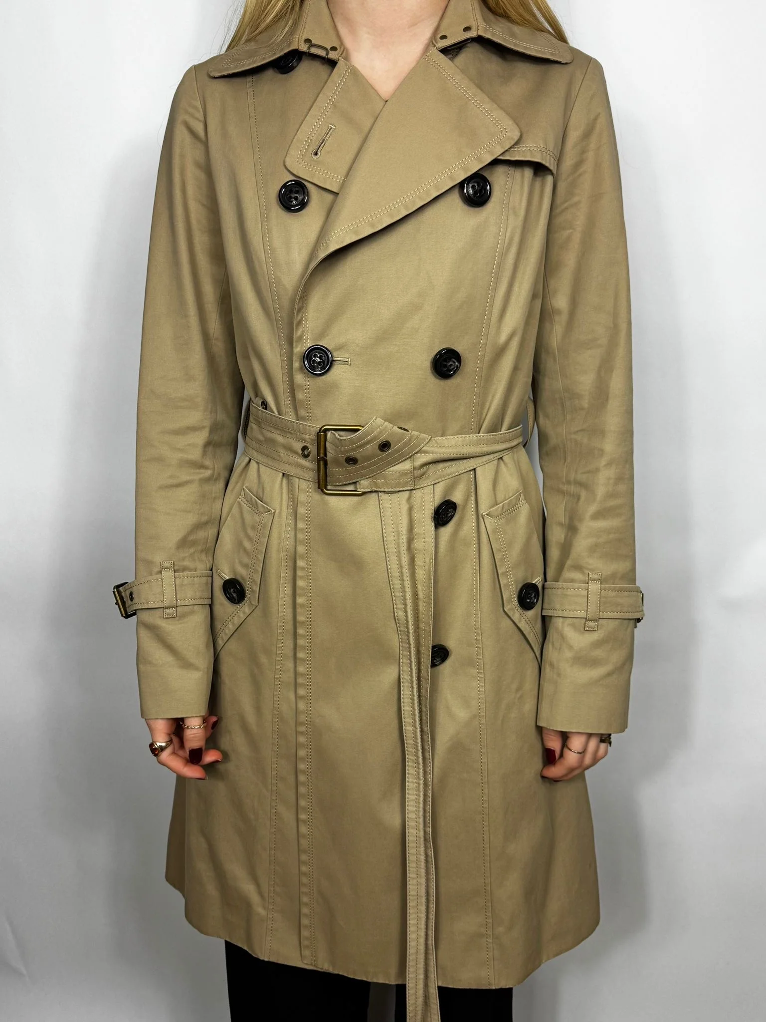 Beige trench coat worn by a person on a white background